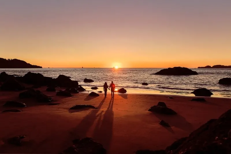man and woman holding hands on beach during sunset