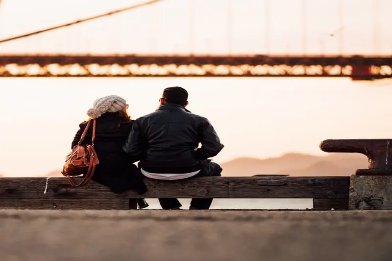 man in black jacket and woman sitting near bridge