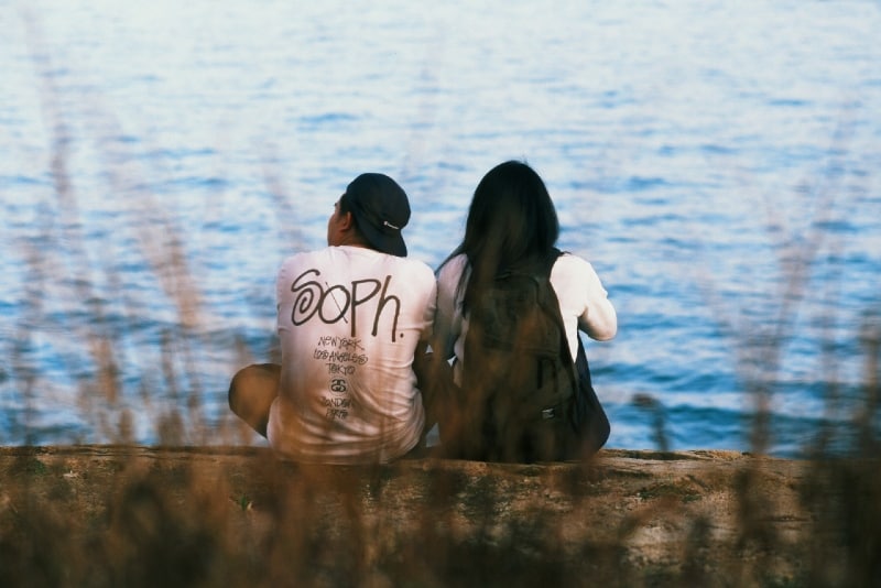 woman with backpack and man sitting near water