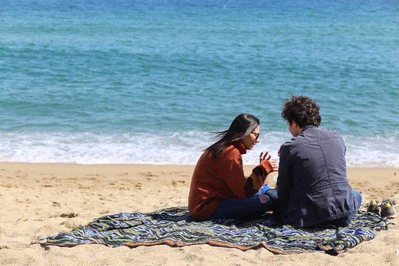 man and woman sitting on blanket on beach near sea