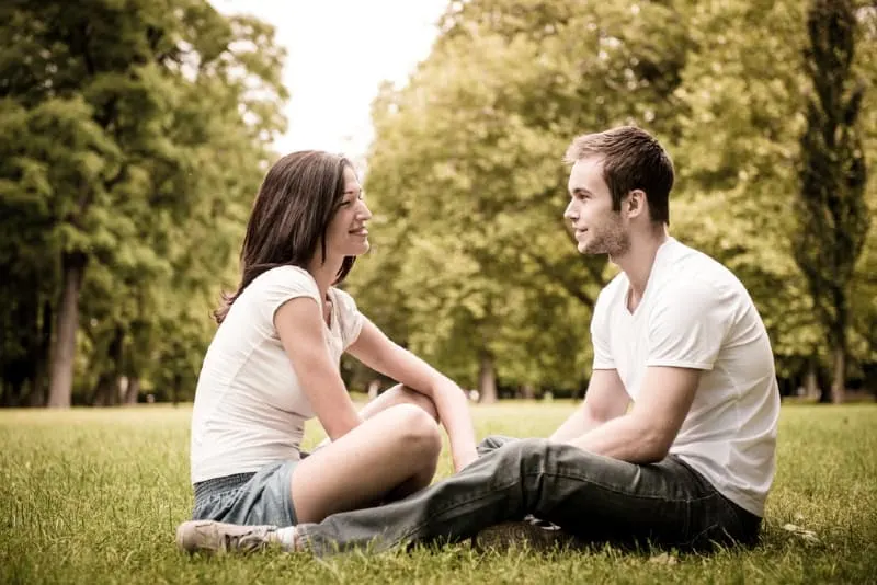man and woman making eye contact while sitting on grass