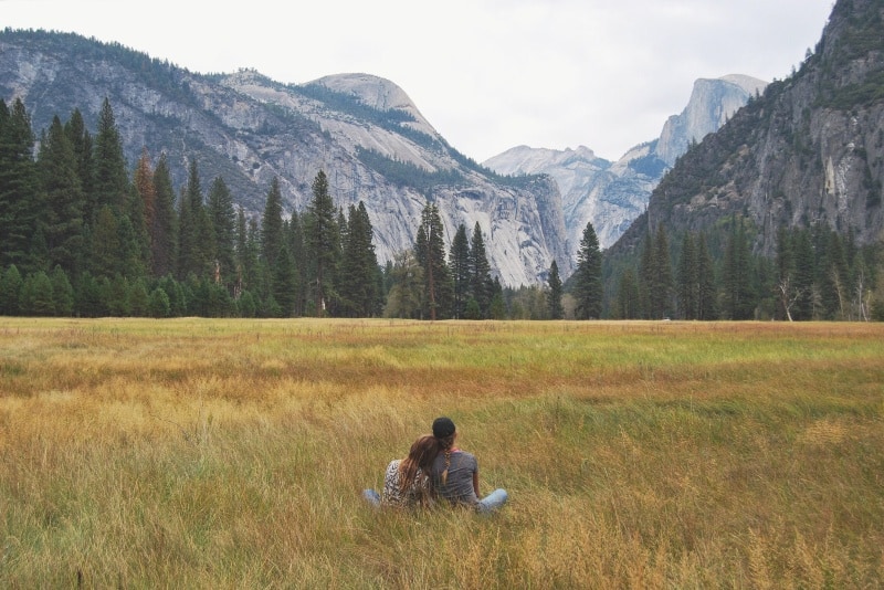 man and woman sitting on grass looking at mountain