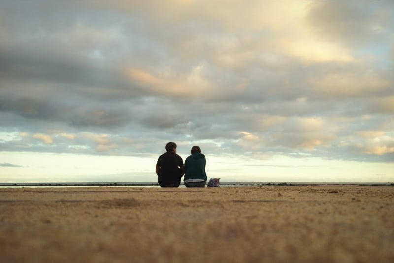 man and woman sitting on ground during sunset