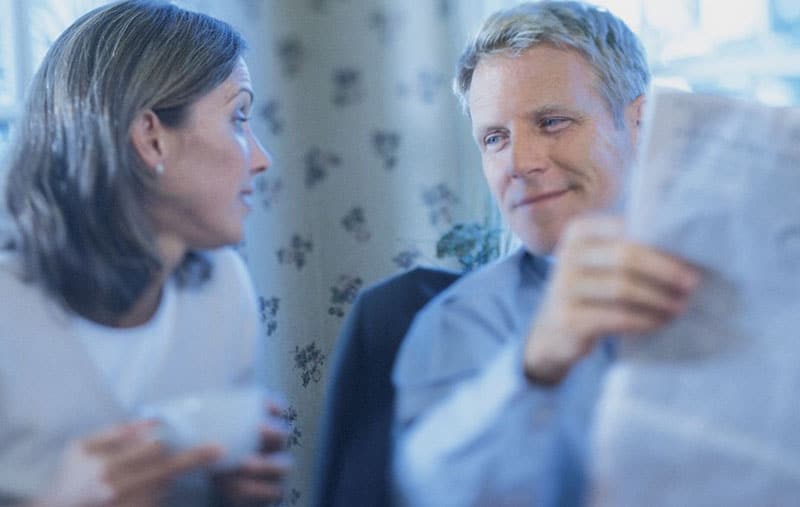 pareja hablando con una taza de café mientras el hombre lee el periódico