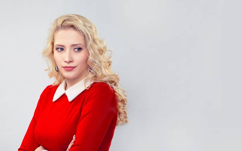 envious young woman standing near the white wall wearing red top