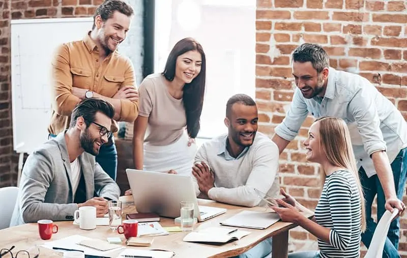 group of cheerful people celebrating success sitting and standing around a table