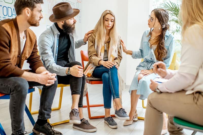 group of people surrounding and consoling a woman while sitting