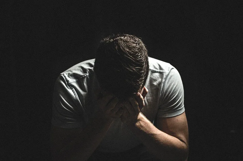 guy crying in the dark while covering his face