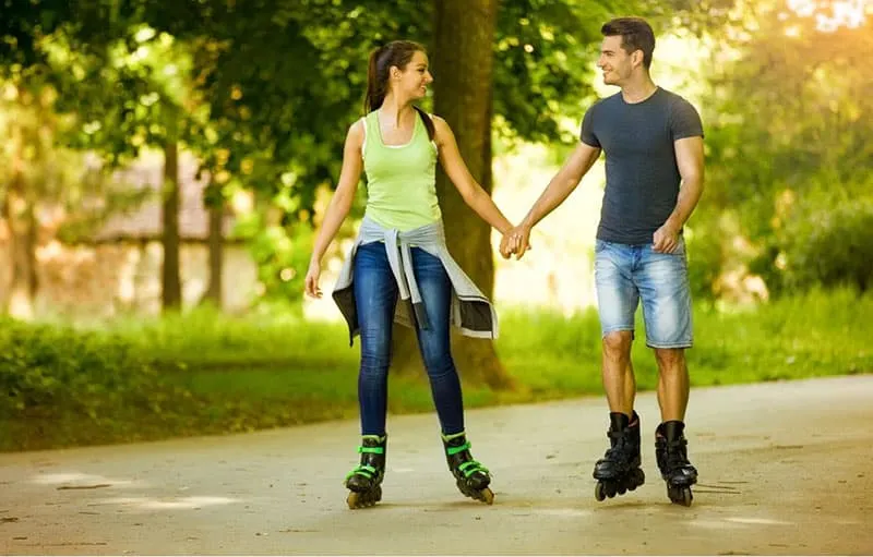 happy couple rollerskating holding hands in the streets of the park