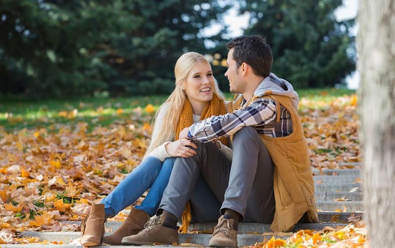 happy couple talking and sitting on the ground with fallen dried leaves