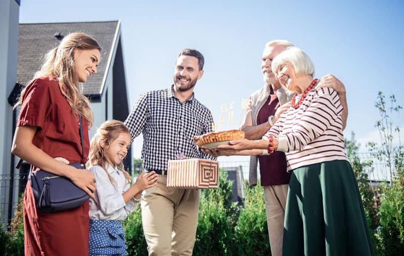 happy young family visiting their mature relatives bringing gifts meeting outdoors
