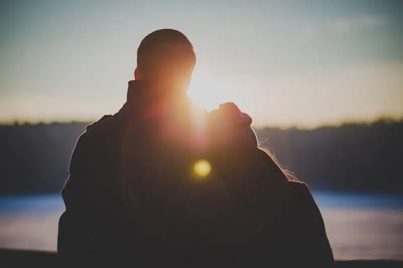 love couple staring sunset facing a body of water