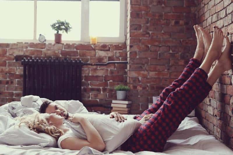 man and woman lying on bed with feet laid against the wall