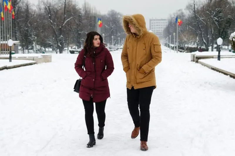 man and woman walking on the snowy streets wearing winter clothes