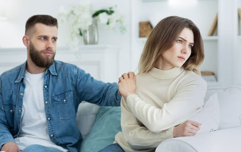 man consoles a woman having problem sitting in the couch