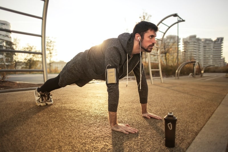 hombre con chaqueta gris haciendo flexiones al aire libre