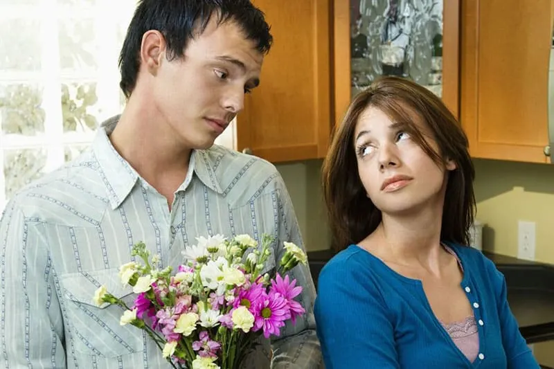 man giving flowers to a woman turning her back but looking at the man inside home
