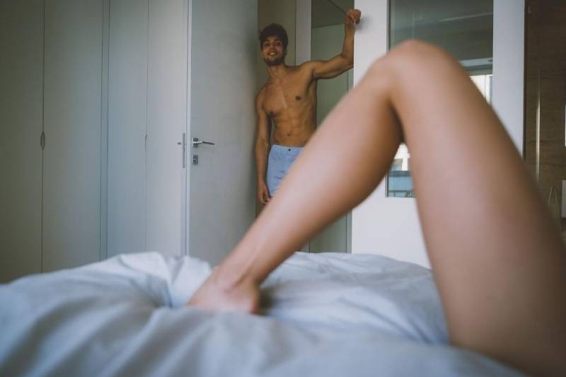 man half naked looking at the woman showing legs on the bed
