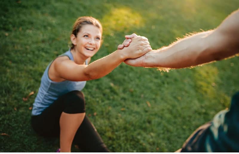 man helping his girlfriend stand up from the ground wearing an athletic wear