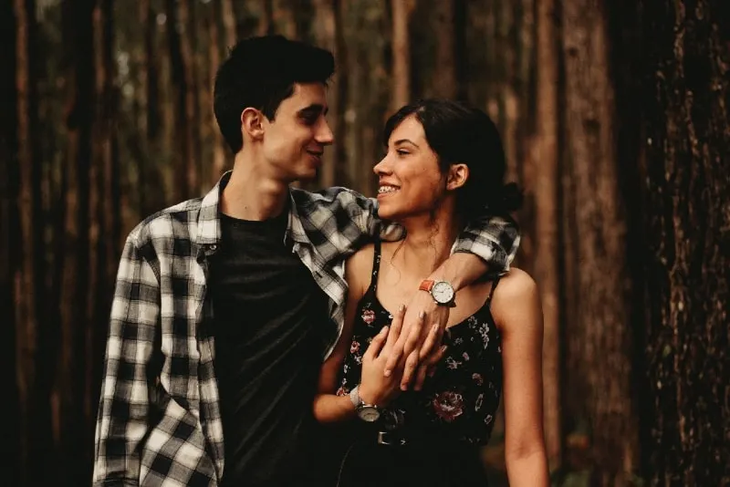 man hugging woman while standing in forest