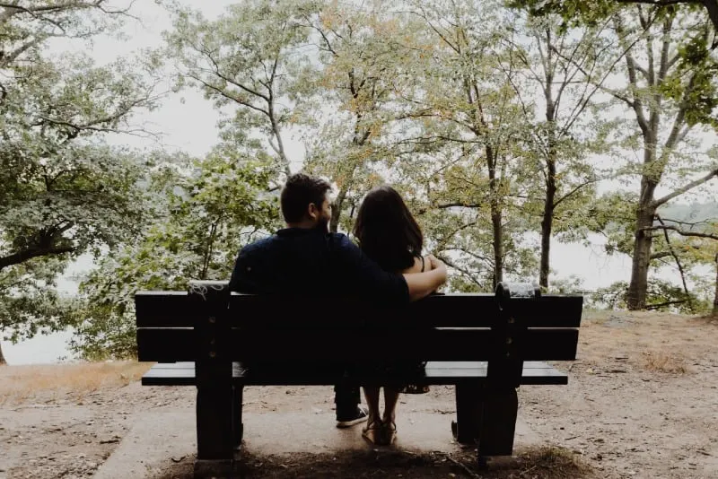 man hugging woman while sitting on bench