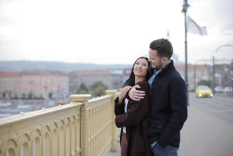man hugging woman while standing on bridge