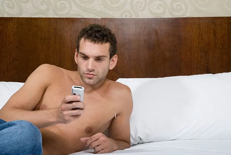 man in topless texting while lying on the bed