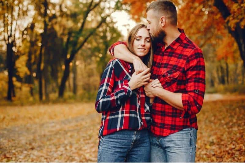 man kissing woman's forehead hugging her in the park