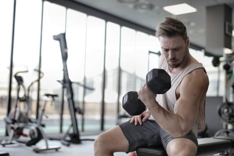 man in white top lifting dumbbell