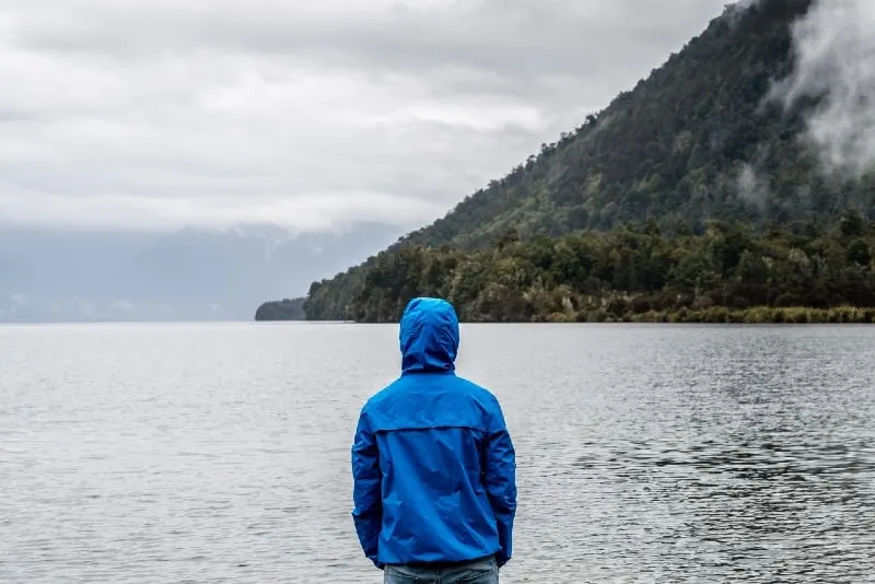 man in blue hoodie looking at lake