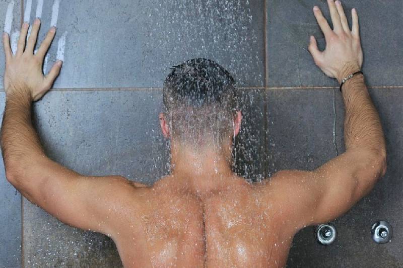 man naked showering with hands turning back