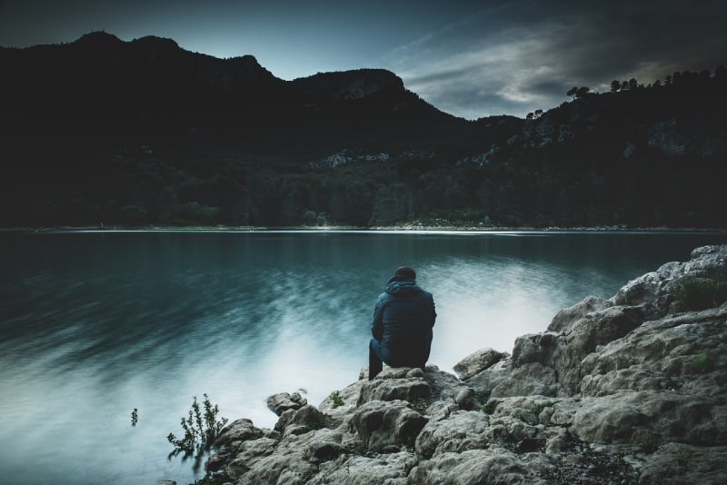 homem sentado perto de um lago a olhar para a montanha