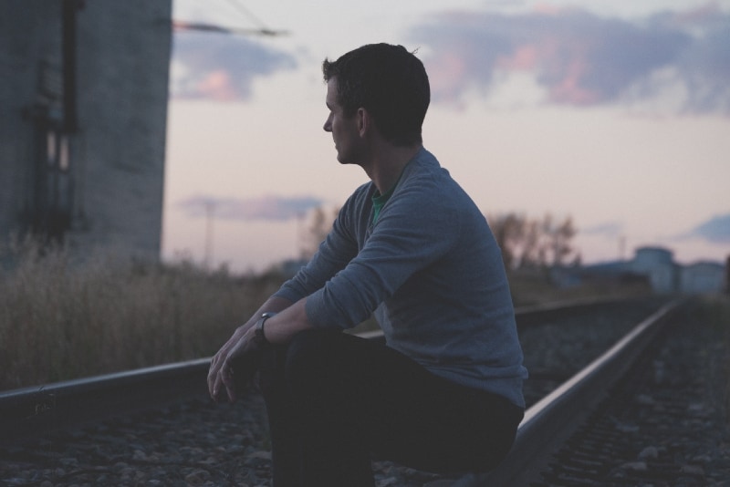 uomo seduto sulla ferrovia sotto un cielo grigio