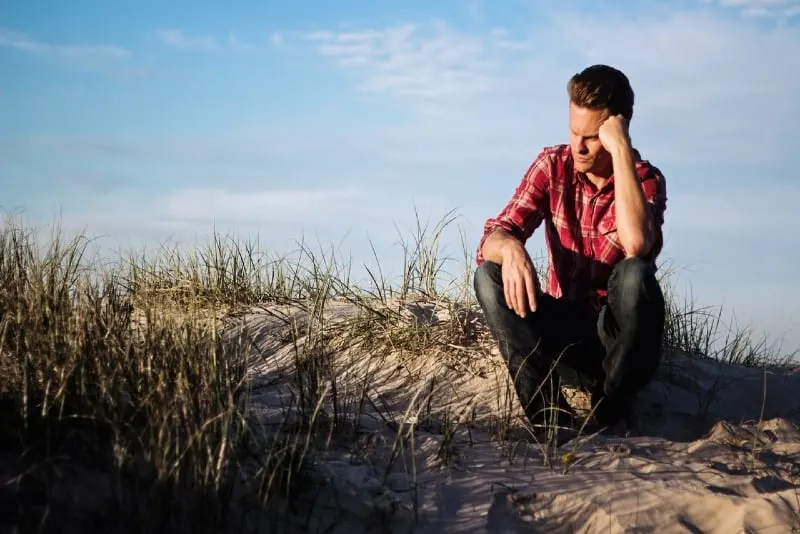 sad man in red checked shirt sitting on sand
