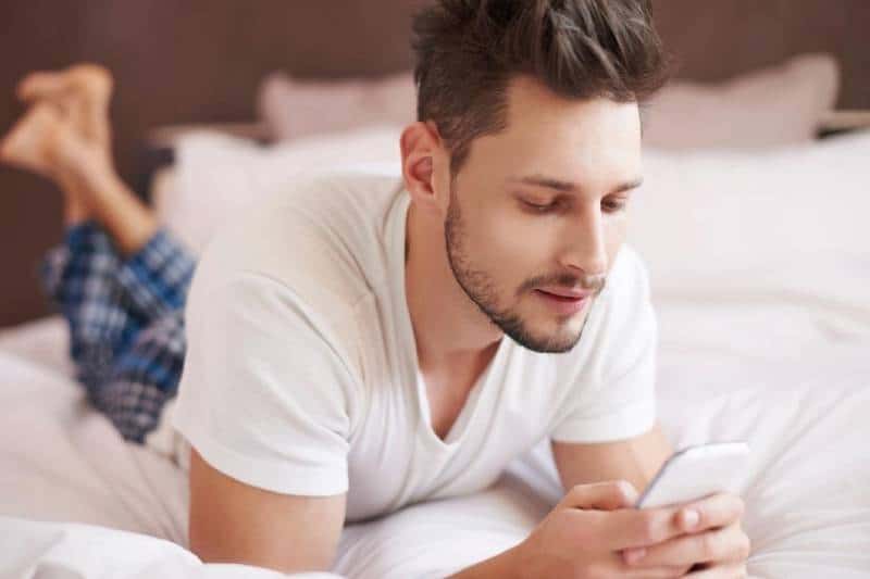 hombre escribiendo en la cama en pijama