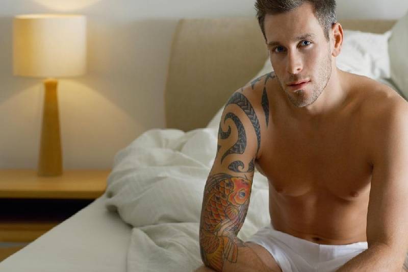 man with tattoo in his arm sitting naked on bed