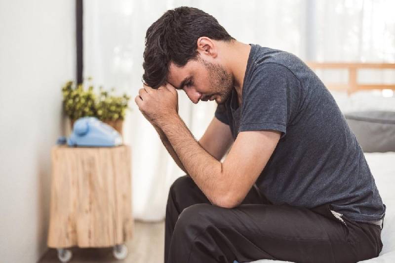 uomo in introspezione a letto a faccia in giù con la mano che sostiene la testa