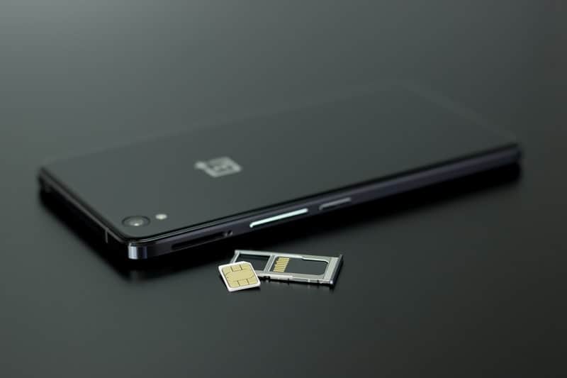 oneplus smartphone black and white placed on the black table with sim cards out of the phone