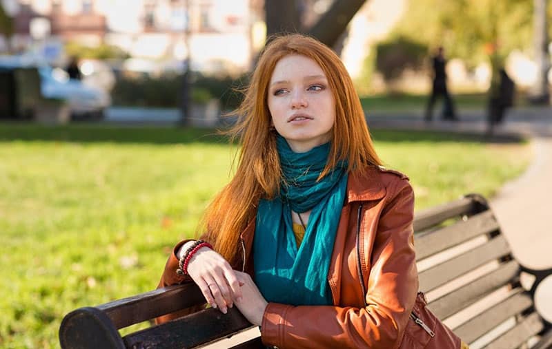 mulher com ar pensativo, usando um lenço verde, sentada num banco de jardim