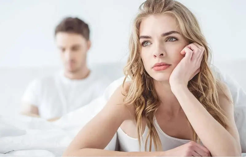 pensive woman in the bed hand supporting head with man at her back near the bed header