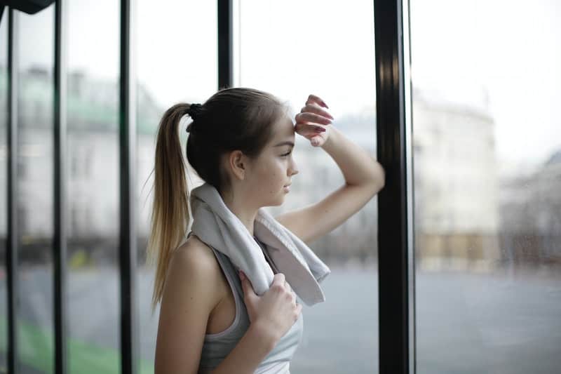 joven pensativa mirando a través de la pared de cristal con ropa deportiva