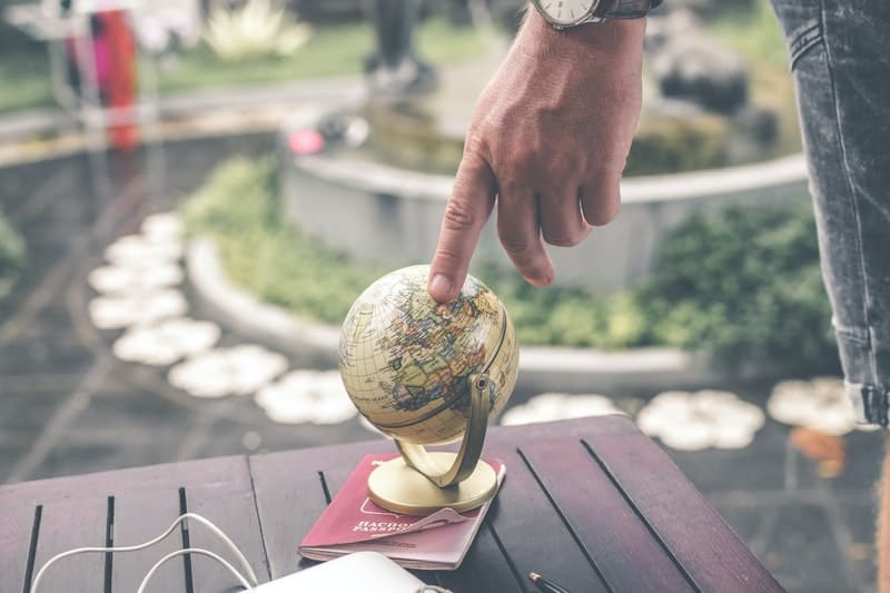 persona que sostiene la maqueta del globo terrestre colocada encima del libro colocado sobre una mesa