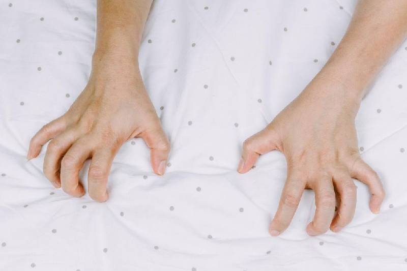 person's hand grasping bed as a sign of orgasm
