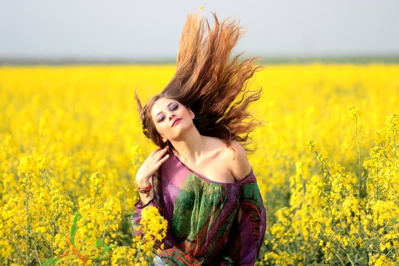 portrait of young woman with yellow flowers on the fields flipping hair 
