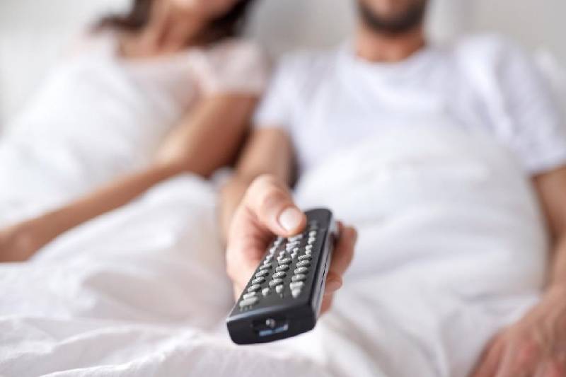 remote control held by a man sitting beside next to a woman