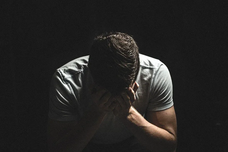 sad guy crying in the dark covering his face with his hands