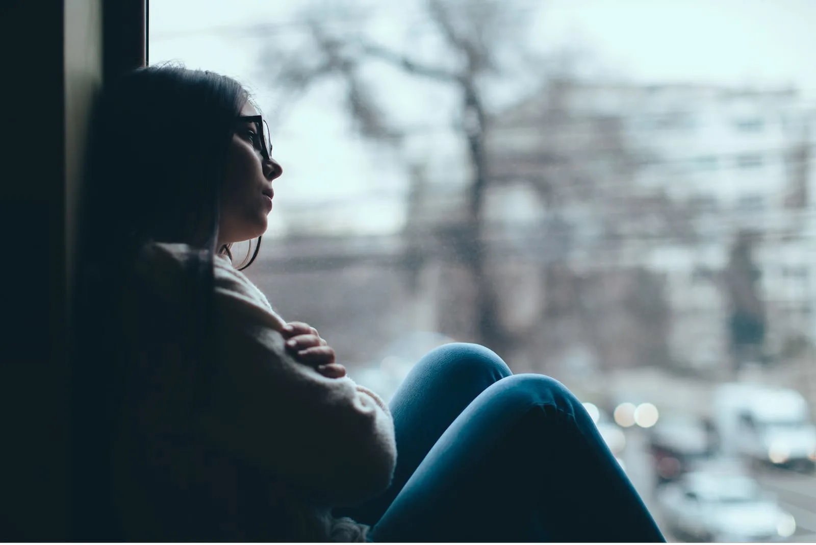 sad woman with glasses sitting by the window