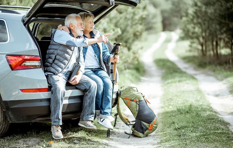 senior people travelling by car sitting on the trunk pointing on something