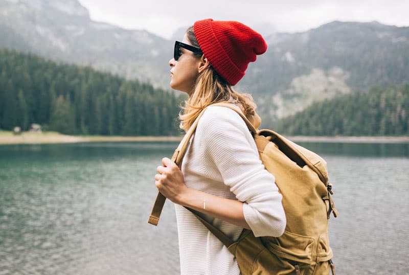 sideview of a woman with backpack with red bonnet exploring a new place near a body of water