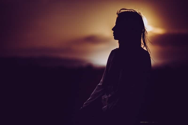 silueta de una mujer sentada durante la puesta/salida del sol en una vista lateral